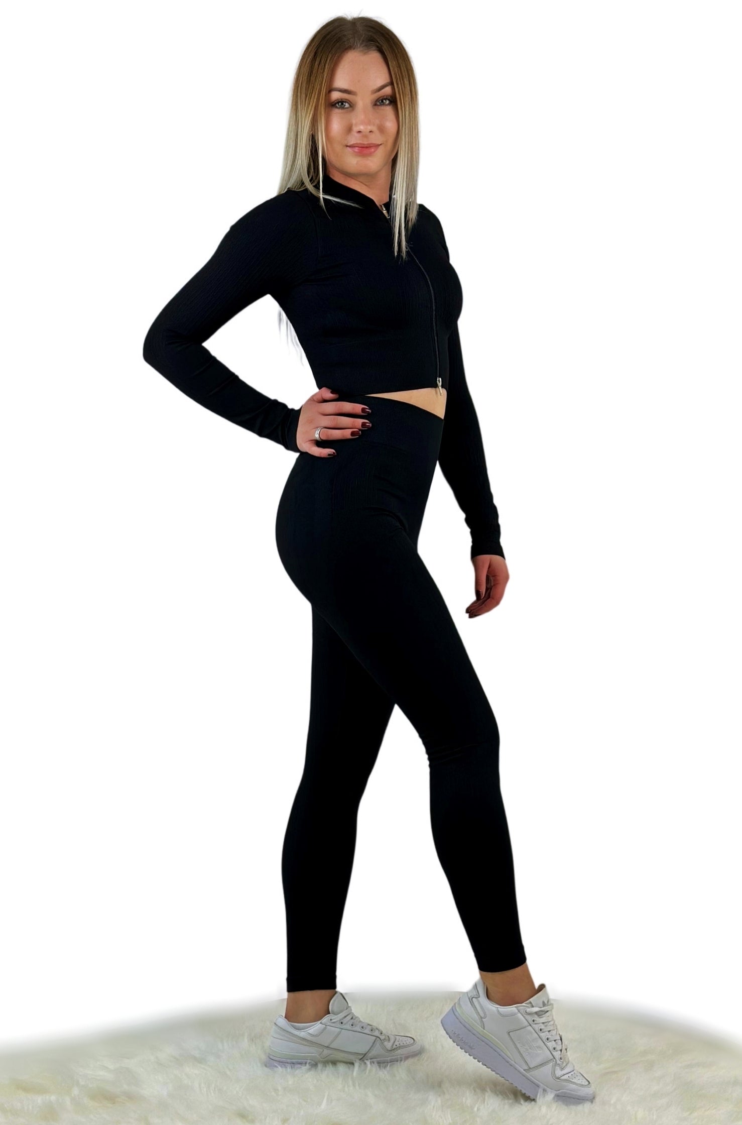 Schwarzes Sport Set für Frauen mit Reißverschluss am langärmligen Oberteil und anschmiegsamer High Waist Leggings. Activewear aus der Tribute Kollektion, bestehend aus hochwertigem Spandex/Nylon mit gerippter Oberfläche. Die Kollektion bietet einen eleganten Look für sportliche Aktivitäten und den Alltag, ist atmungsaktiv, nahtlos, reversibel und feuchtigkeitsabweisend. Verfügbar in drei stylischen Farboptionen